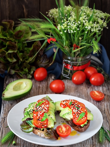 Free photo two sandwiches with freshly baked bread, olive oil, lettuce, avocado, sesame seeds and cherry tomatoes on a white plate