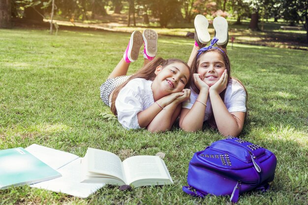 Two schoolgirls lying on grass with heads propped in hands smiling