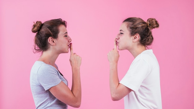 Free Photo two sister standing face to face showing silence gesture to each other