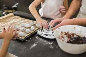 Free photo two sisters and mother preparing chocolate cookie in kitchen