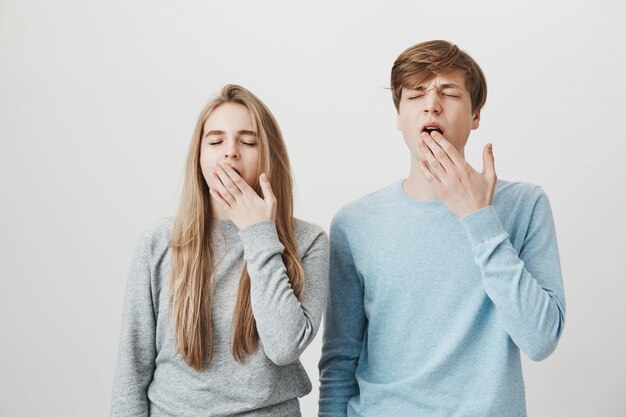 Two sleepy friends yawning. Blond girl and guy cover mouth, feel bored