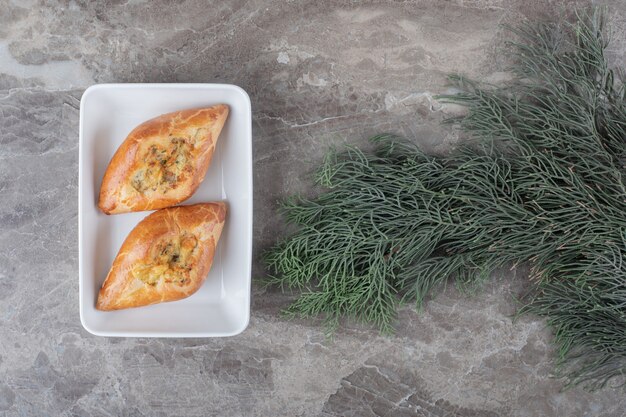 Two small turkish pides on a platter next to pine branches on marble surface