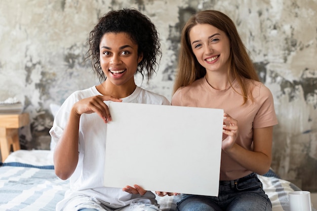 Two smiley friends holding blank placard in bed