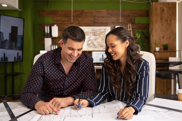 Two smiling architects sit at a table and discuss a new project. Modern office and blue print