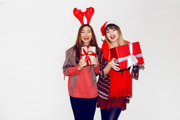 Two smiling women holding new year gifts. Wearing cute masquerade hats. Candid smile. Celebrating mood. Flash portrait.