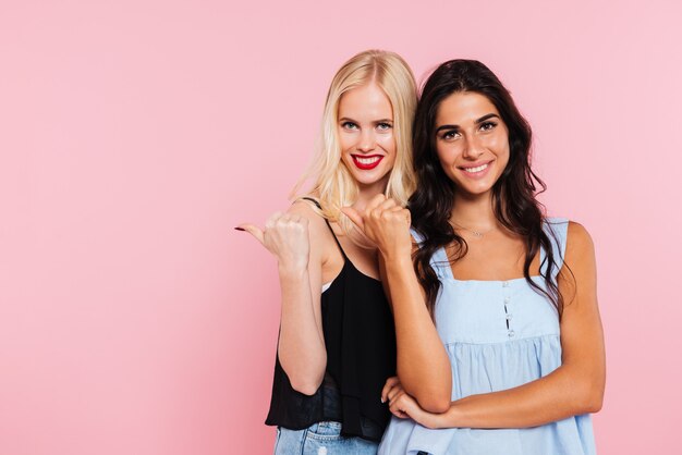 Two smiling women pointing away and looking at the camera