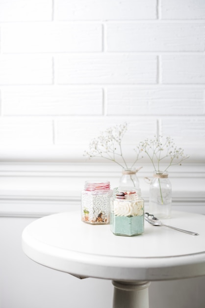 Free Photo two smoothies glass jars with spoon on table against white wall