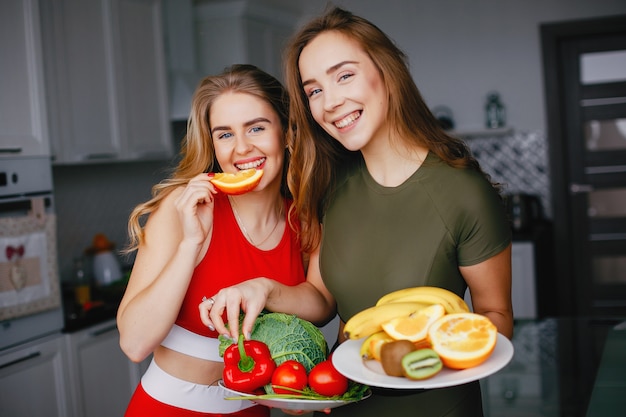 Two sports girl in a kitchen with vegetables