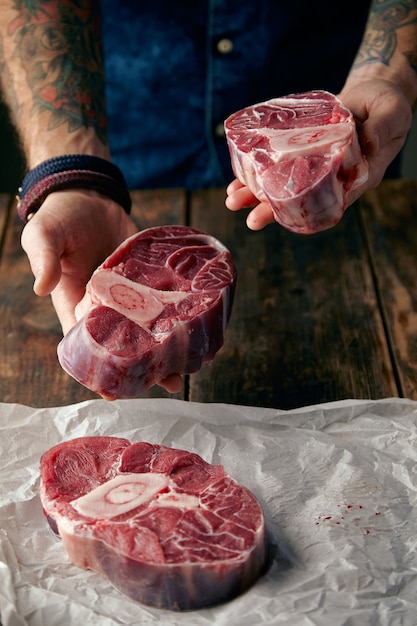 Two steaks in tattooed hands and other on craft paper. Offer to buy meat on camera.