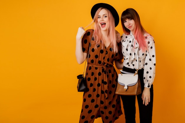 Two stylish elegant women in dresses posing over yellow wall