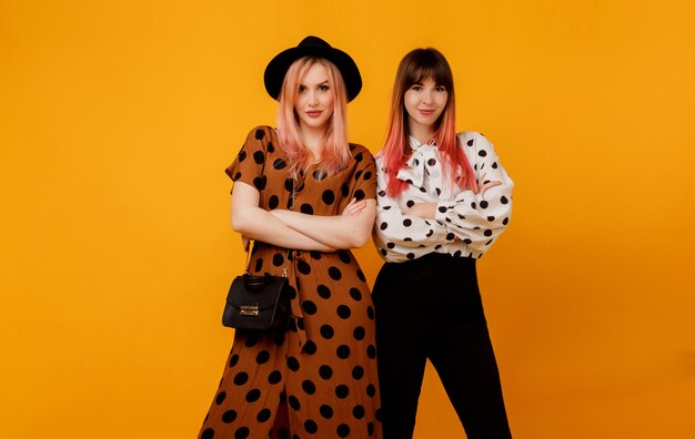 Two stylish elegant women in dresses posing over yellow wall