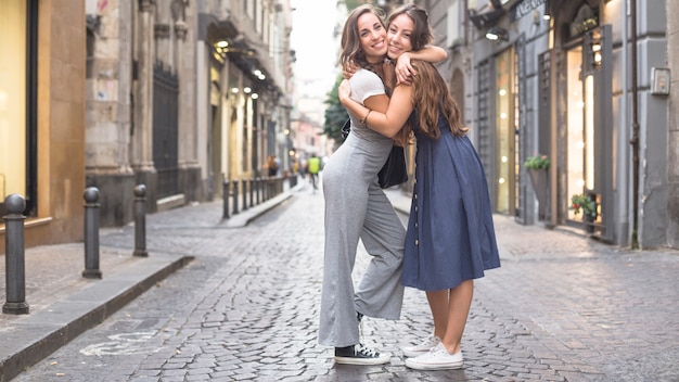 Free Photo two stylish female friends standing on street hugging each other