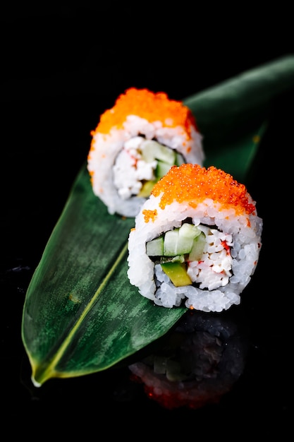 Two sushi rolls on a green leaf in black space.