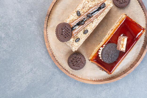 Two sweet delicious piece of cakes with cookies on wooden board