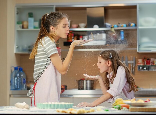 Two teenage girls having fun in the kitchen when making the dough.