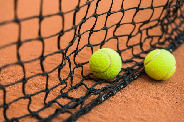 Two tennis ball near the black net on ground