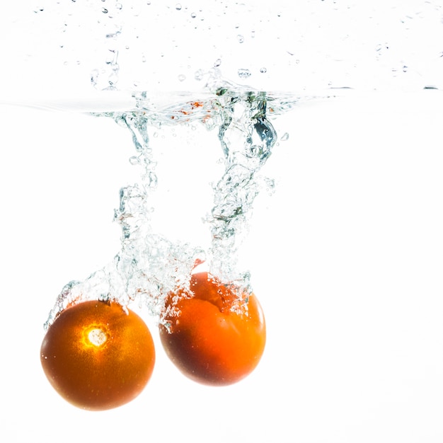 Two tomato falling into the water over white background