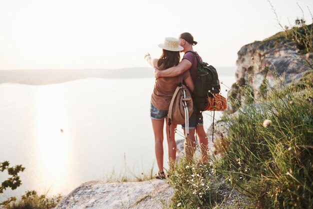 Two tourist male and woman with backpacks stand to the top of the crag and enjoying sunrise.