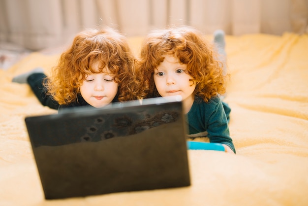 Two twins lying on bed looking at laptop