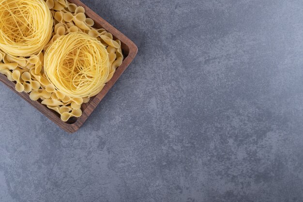 Two types of raw pasta on wooden board.