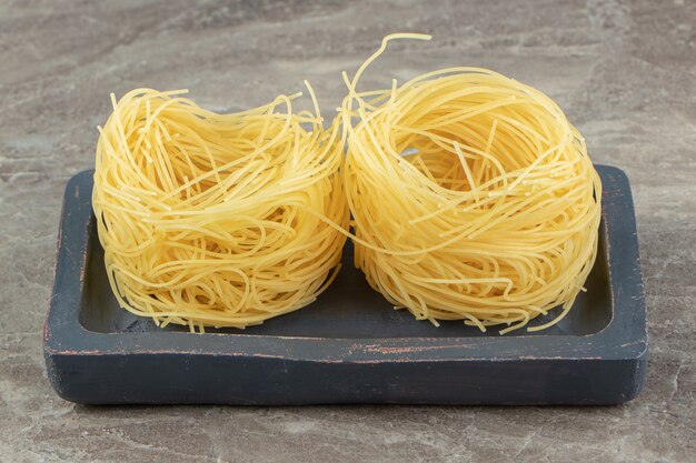 Two uncooked noodle nests on black plate