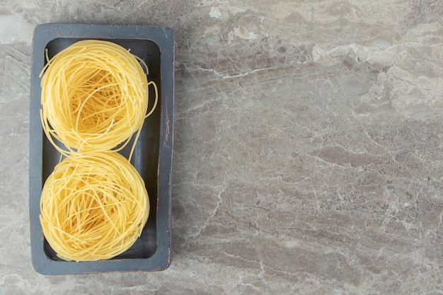 Two uncooked noodle nests on black plate.