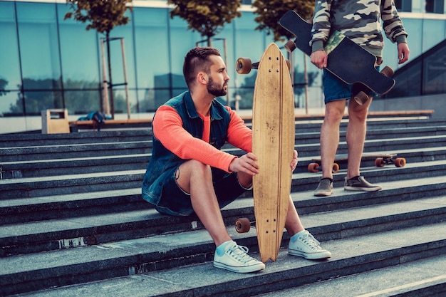 Free photo two urban males posing with longboard on steps in downtown.