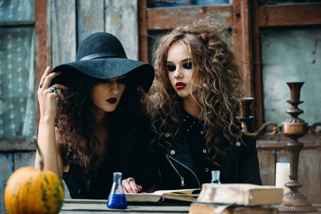 Two vintage witch sitting at the table in an abandoned place on the eve of Halloween