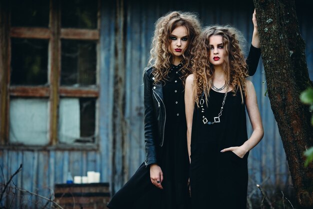 Two vintage women as witches, posing beside an abandoned building on the eve of Halloween