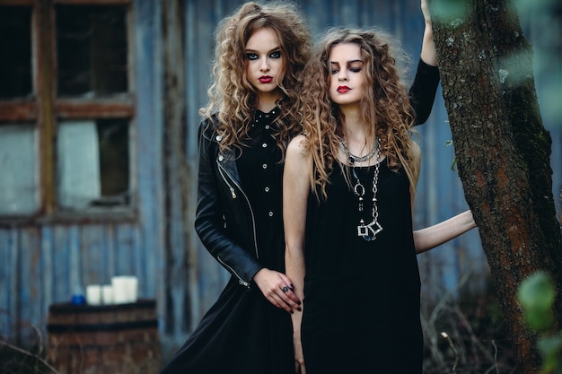 Two vintage women as witches, posing beside an abandoned building on the eve of Halloween