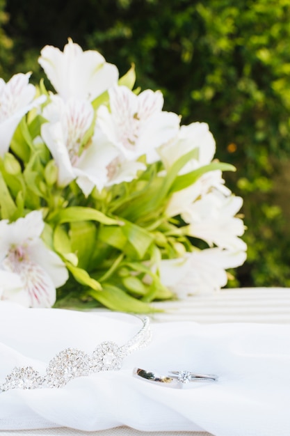 Two wedding rings and crown on scarf with beautiful flower bouquet over table