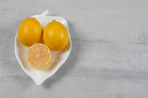 Two whole and a half lemon in the plate on the marble surface