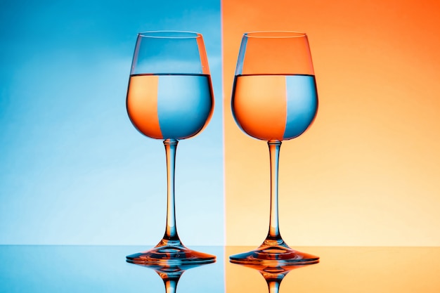 Two wineglasses with water over blue and orange background.