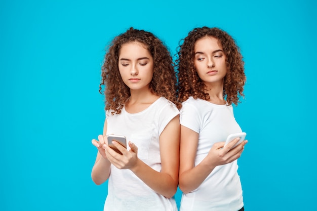 Free Photo two womans twins looking at phones over blue.