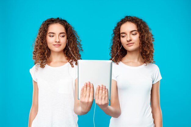 Free Photo two womans twins looking at tablet, smiling over blue.