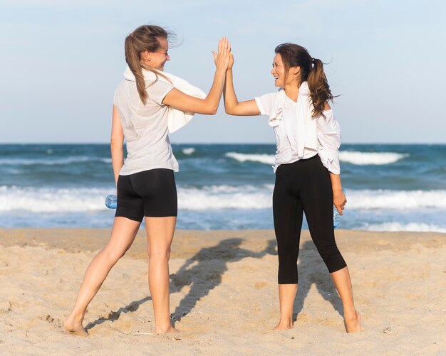 Two women high-fiving while working out on the beach