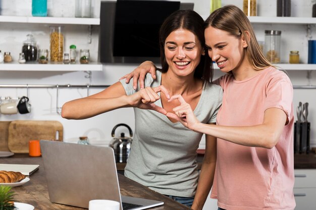 Two women at home showing heart while video chatting