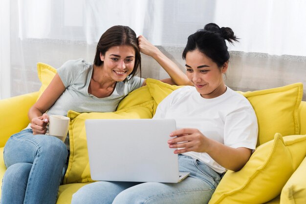 Two women at home using laptop on couch