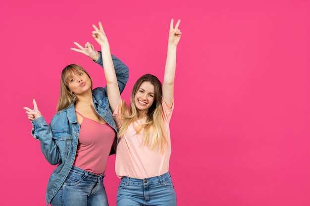 Two women with hands raised on pink background