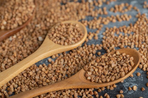 Two wooden spoons full of raw buckwheat