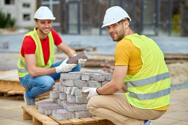 Free photo two workers stacking bricks looking at camera