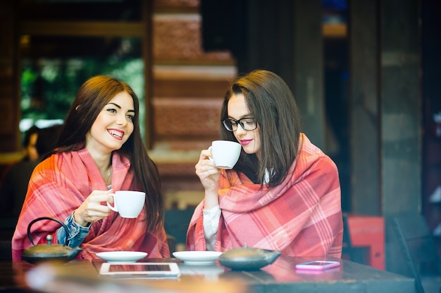 Two young and beautiful girls gossiping on the terrace with a cup of coffee