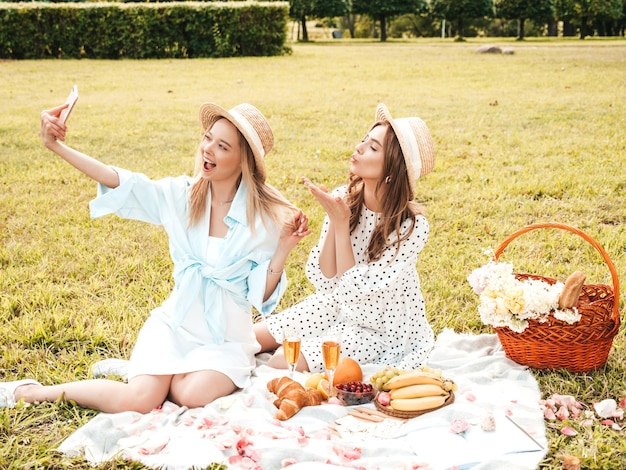 Free photo two young beautiful hipster woman in trendy summer sundress and hats. carefree women making picnic outside.