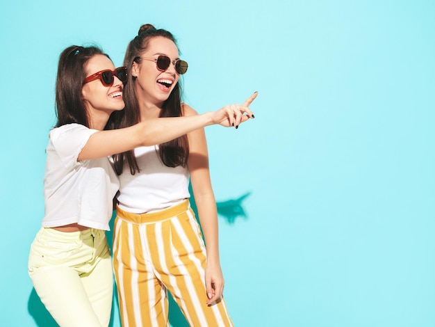 Two young beautiful smiling blond hipster female in trendy summer clothes Sexy carefree women posing  in studio Positive models having fun Cheerful and happy