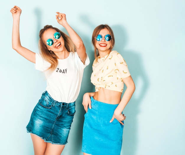 Two young beautiful smiling blond hipster girls in trendy summer colorful T-shirt clothes. 