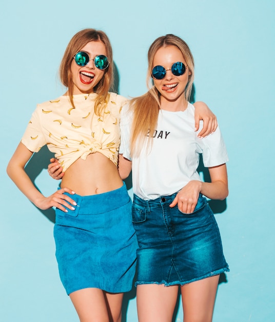 Two young beautiful smiling blond hipster girls in trendy summer jeans skirts clothes.  and showing peace sign