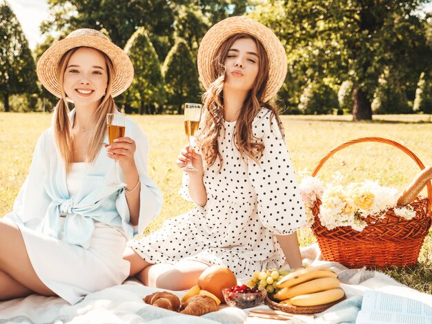 Two young beautiful smiling hipster female in summer sundress and hats.Carefree women making picnic outside.