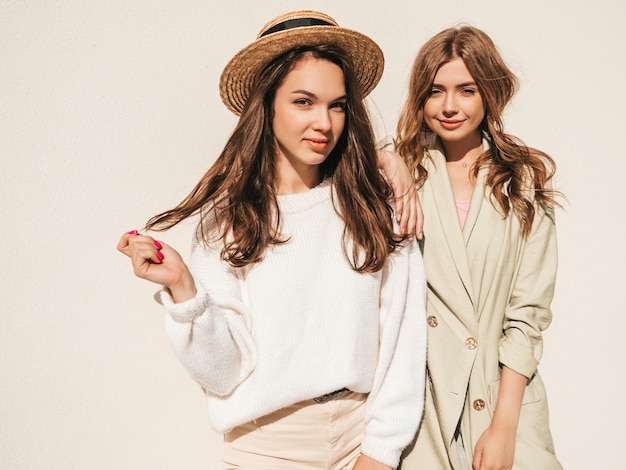 Two young beautiful smiling hipster female in trendy white sweater and coat