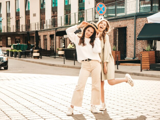 Two young beautiful smiling hipster female in trendy white sweater and coat