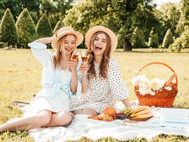 Two young beautiful smiling hipster girls in trendy summer sundress and hats.Carefree women making picnic outside.